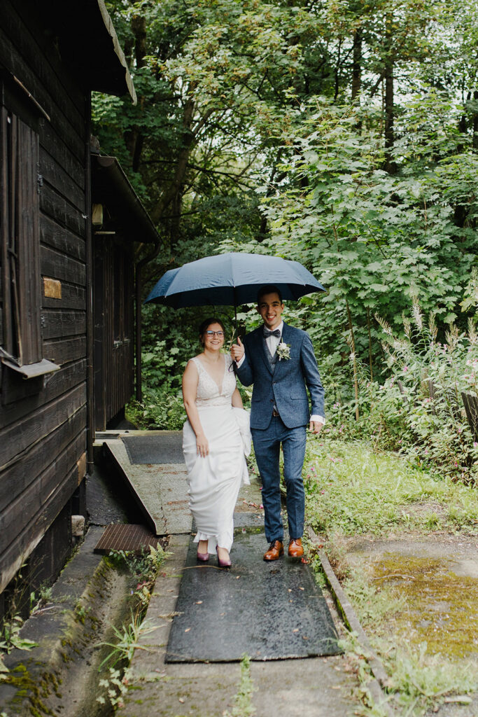 Brautpaar im Regen mit Schirm und Lächeln